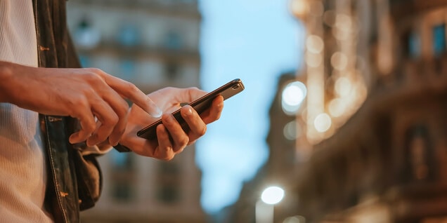 partial view of a man interacting with his phone and the background of the city with buildings and lights.